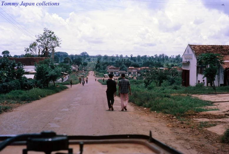 a group of people walking down a dirt road near some houses