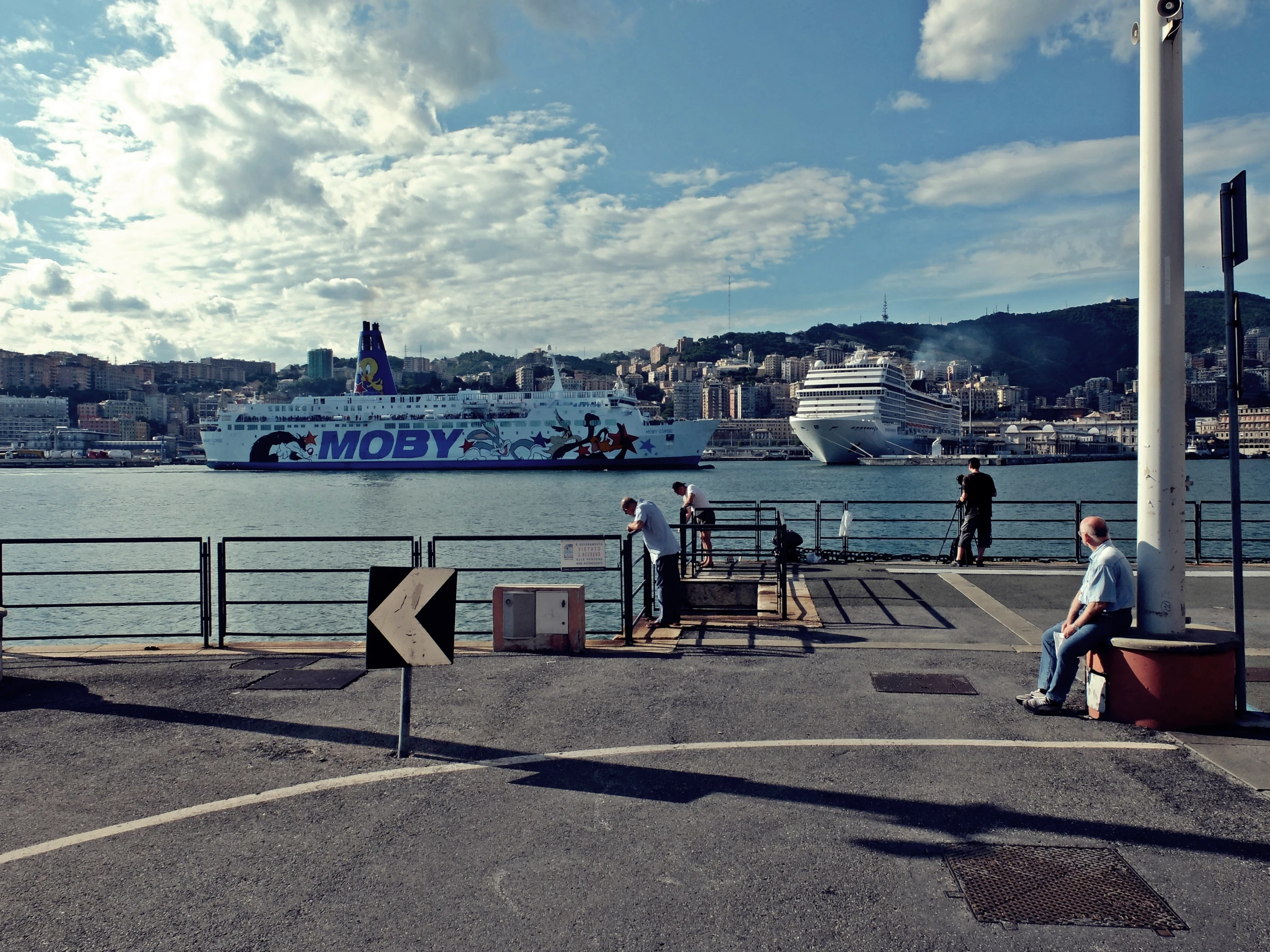 people sit on the steps beside the water with a cruise ship in the background