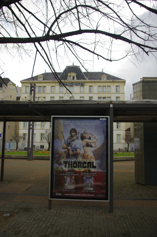 an advertise poster on the side of a sidewalk in front of a building