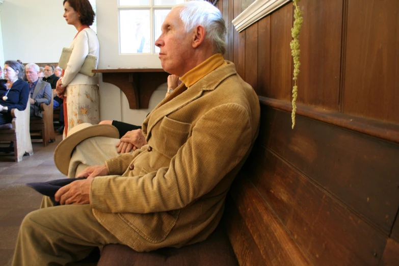 elderly man sitting on bench with several people behind him