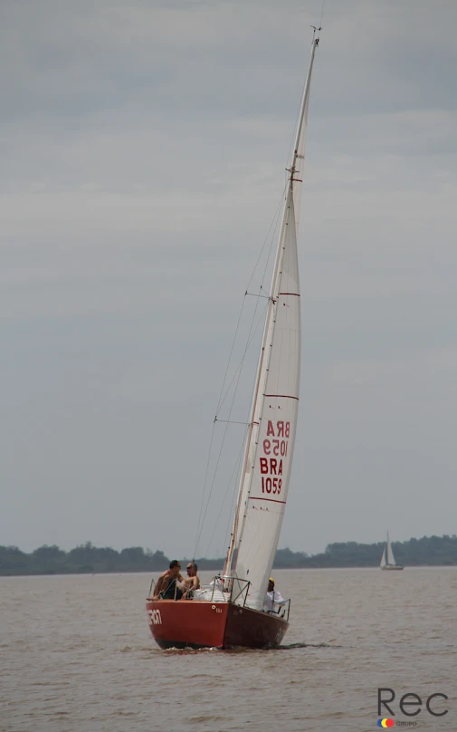 a red sailboat with three people on it in the water