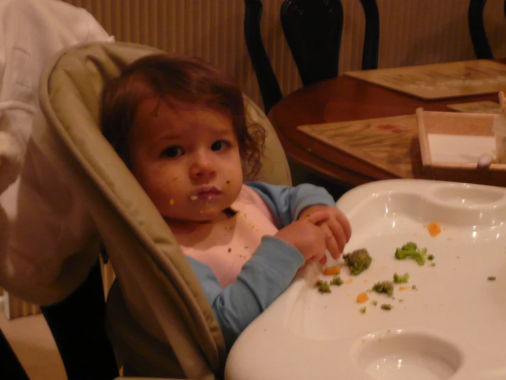 a little girl sitting in her highchair eating broccoli