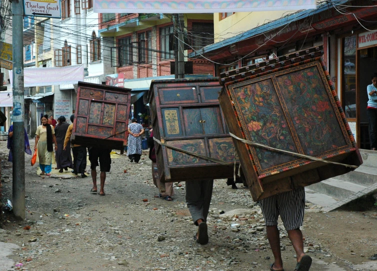 people carrying boxes and other objects down a busy street