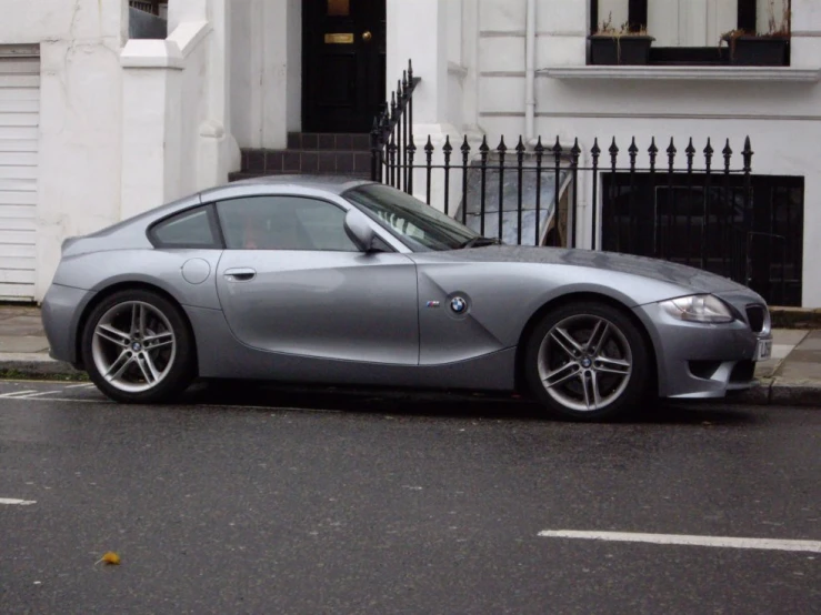 silver sports car parked on the street with a fence behind it