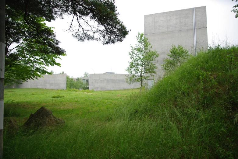 an empty grassy field with several concrete buildings in the background