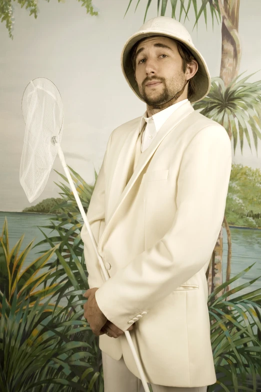 a man dressed in an off - white suit and a top hat holds a stick