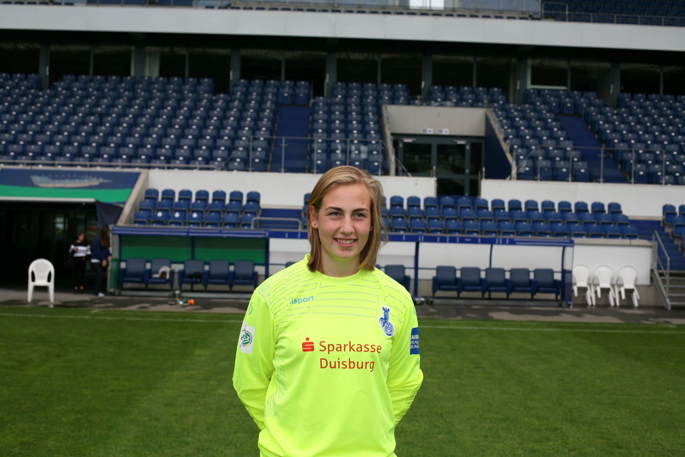 a boy with a yellow shirt standing on a field in front of an empty stadium