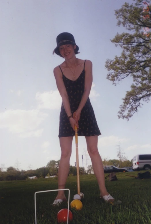 a woman in a black dress and hat holding a croquet
