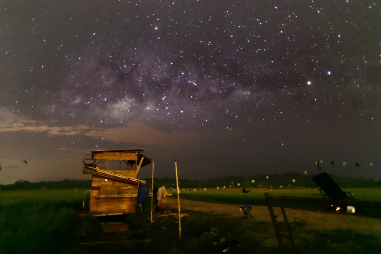 a grassy field with a wooden structure in it under the stars