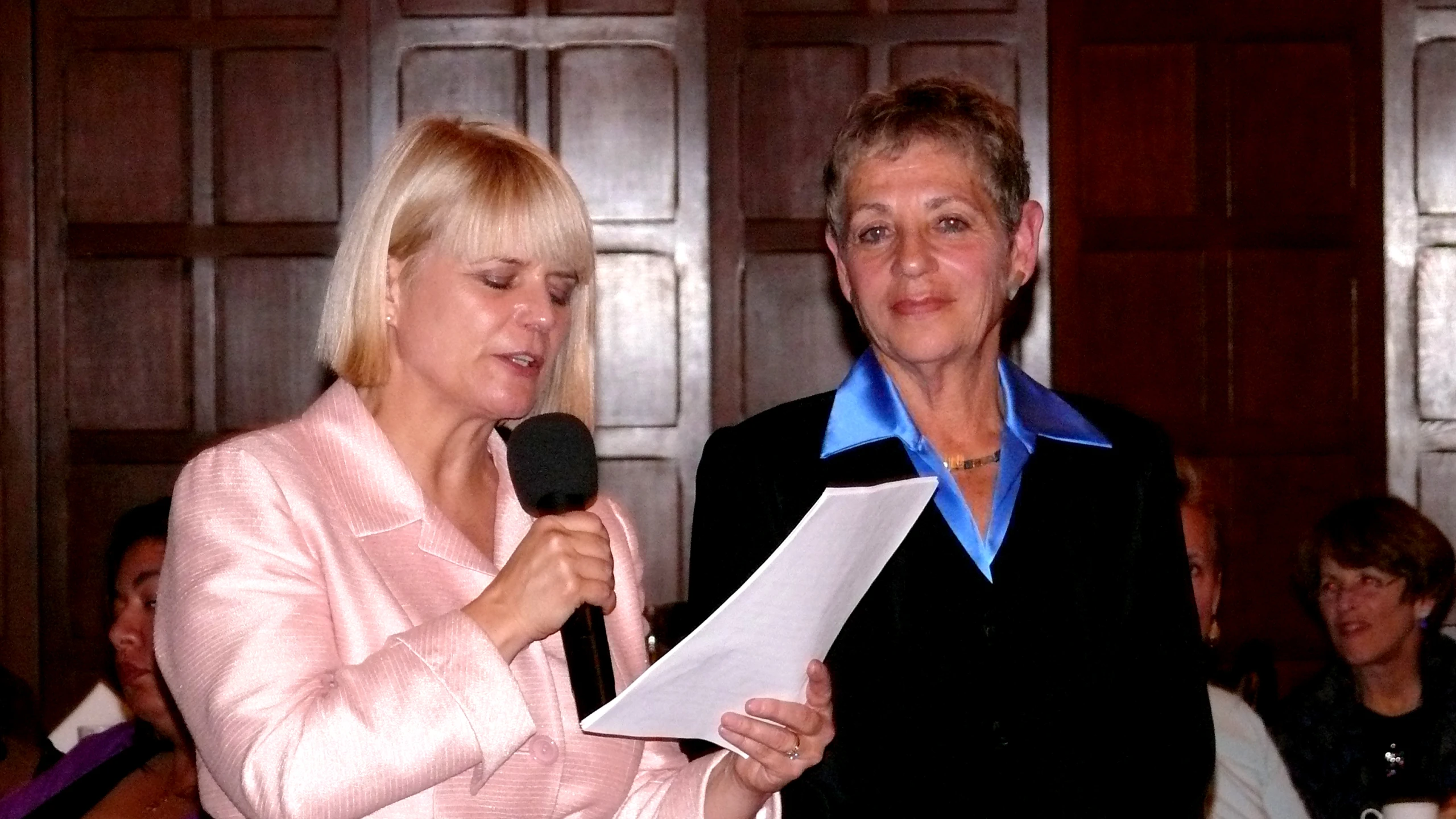 a woman speaking into a microphone while holding a piece of paper