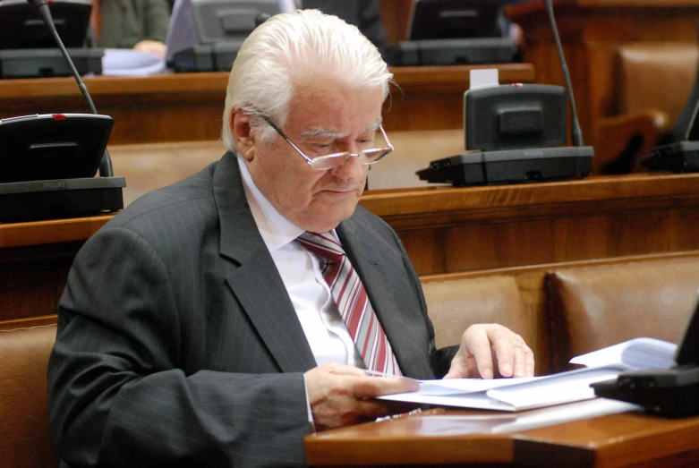 a man in suit and tie writing on paper while sitting in a chair