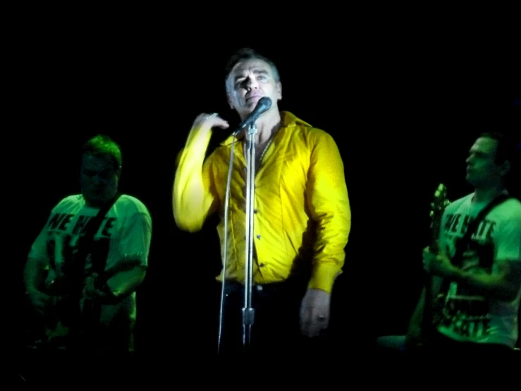 a man singing into a microphone while standing in front of two other men