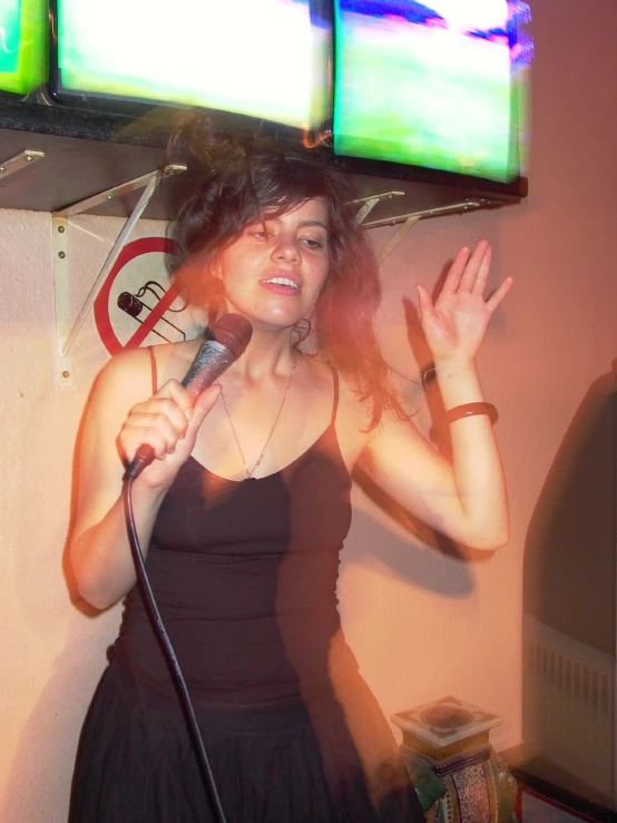 woman singing into microphone under television set with two monitors