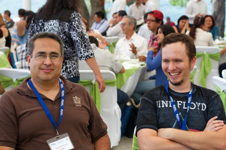 two men in a crowded convention hall, one is wearing a blue necktie and the other wears a brown shirt