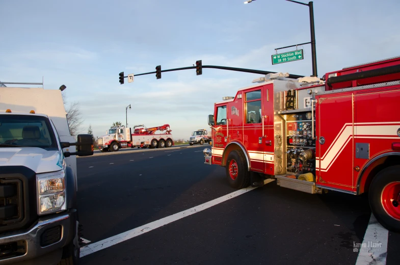 the large red fire truck is on the road beside two other trucks