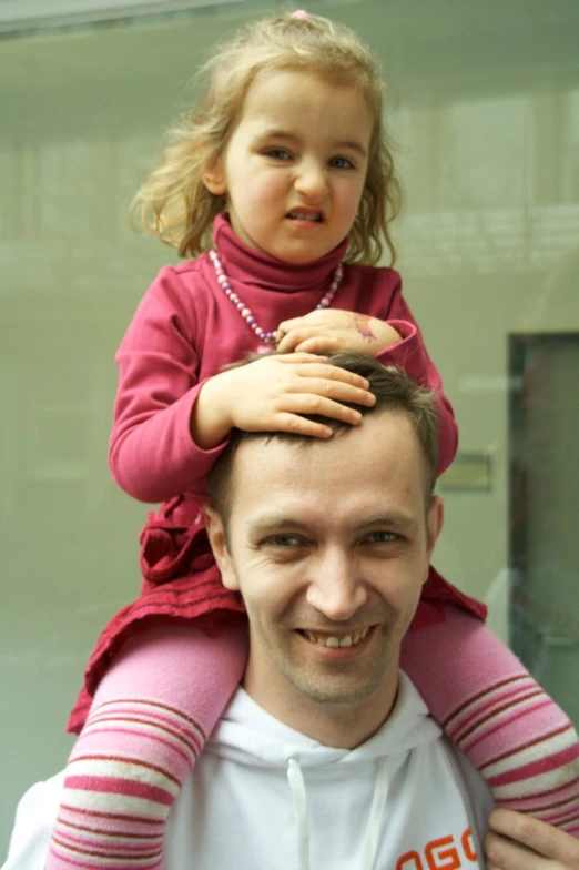 a man smiles as he lifts up a small girl on his shoulders