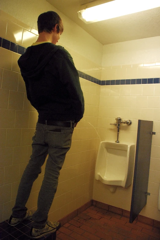 the man standing in the urinals is watching soing