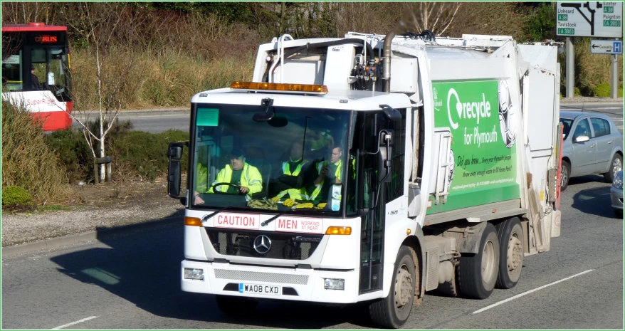 a garbage truck driving down the road with its doors open