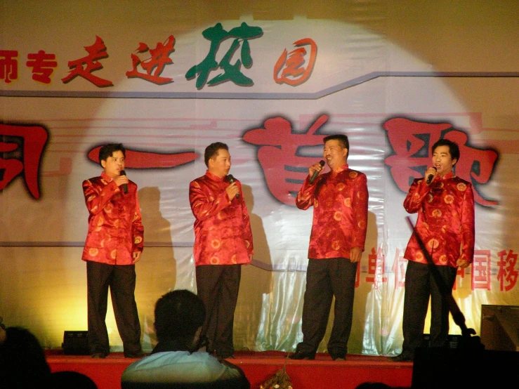 four people in red are singing on stage