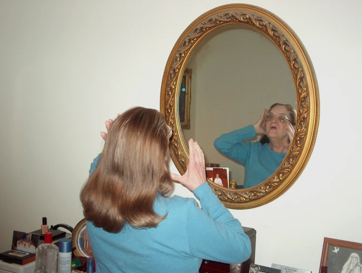 woman wearing blue is looking in a mirror and combing her hair