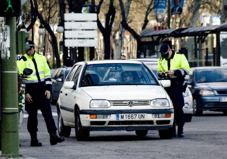 two police officers stand near a parked car