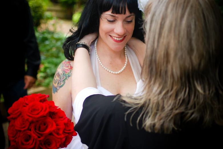 a woman with a flower bouquet and pearl necklace talking to another woman