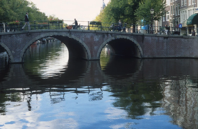 the water is reflecting the old bridge and people on the other side