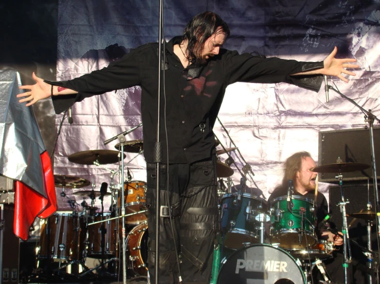 man on stage with his arms outstretched near two drums