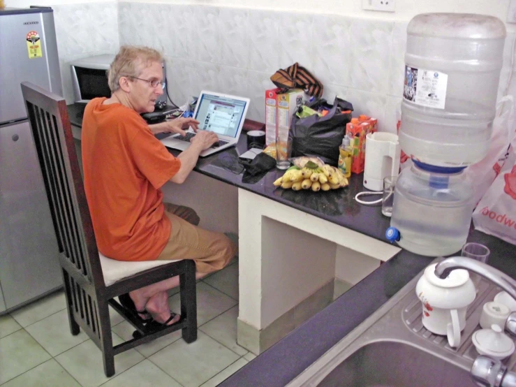 a man is sitting at his computer in the kitchen