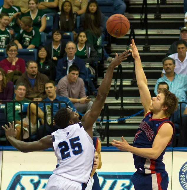 two men playing basketball with a crowd of people watching