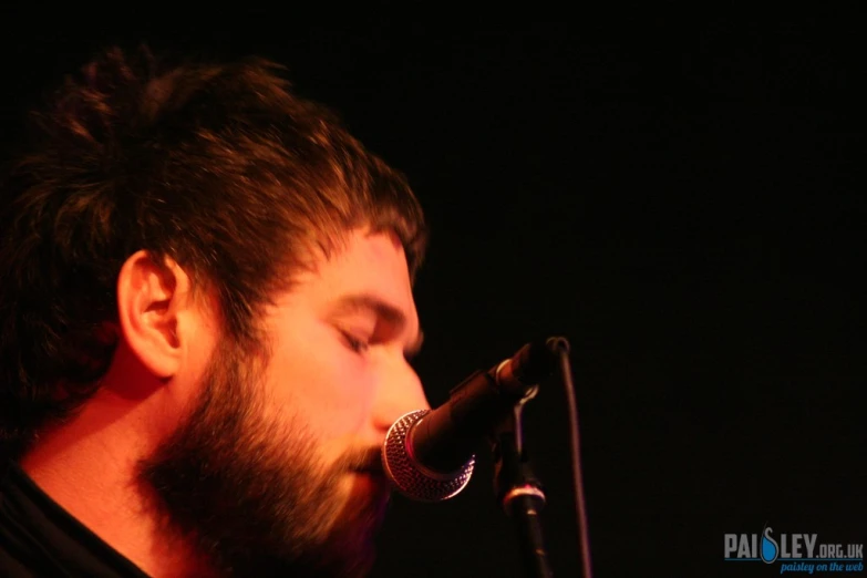 man with beard performing on stage in front of a microphone