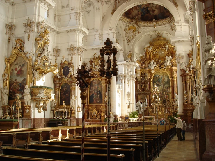 ornately decorated pews and high vaulted ceilings stand beside a wall with paintings on it