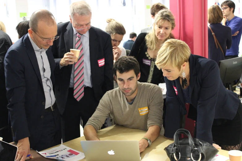 a group of people standing around and looking at a laptop