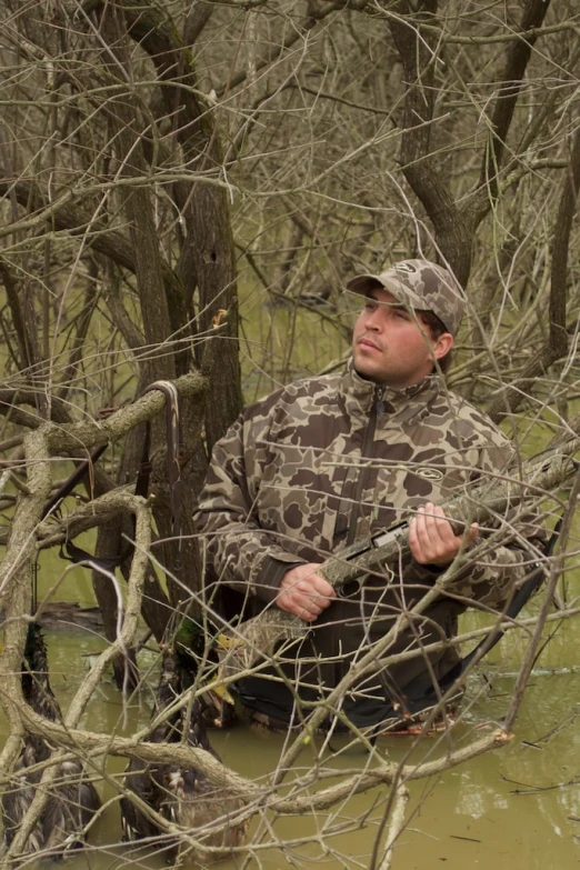 a man sits in the water with his hand in his pocket while holding a hunting gun