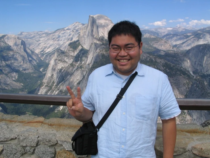 a man in glasses smiles while standing on a high hill