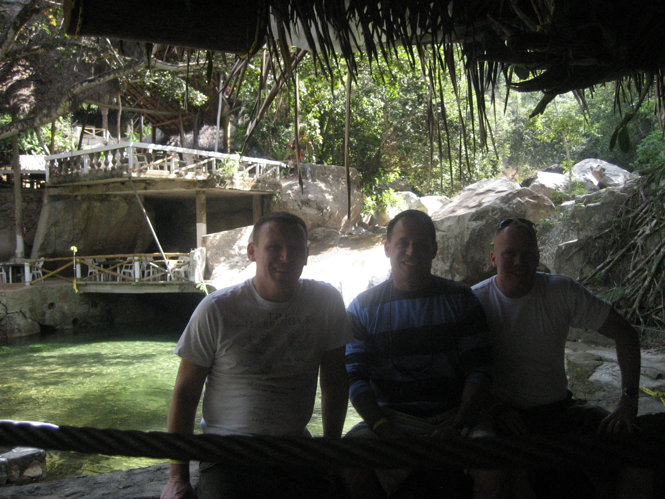 three men smiling near a dock, in front of a boat