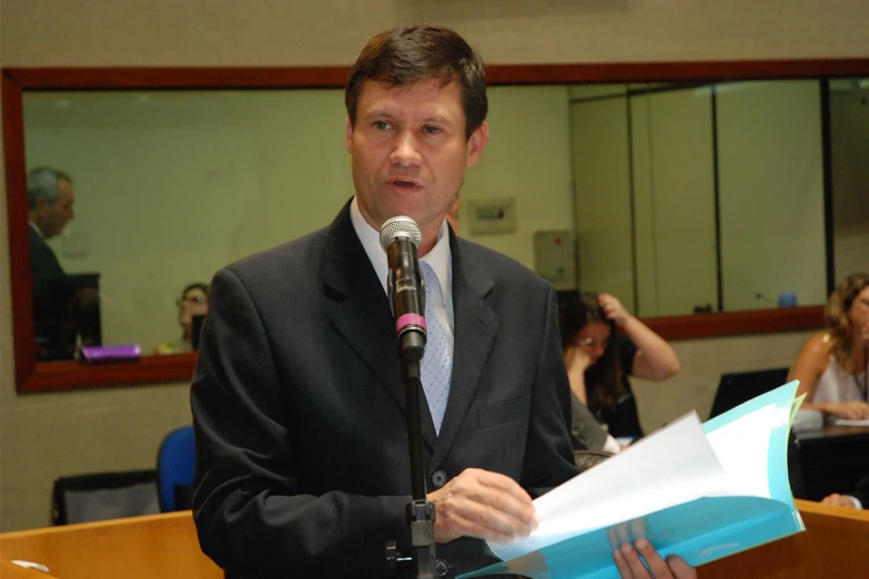 a man speaking into a microphone with a sheet of paper in his hand