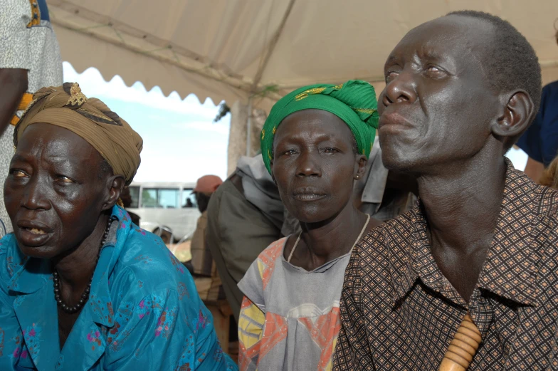 three people sitting next to each other near a tent