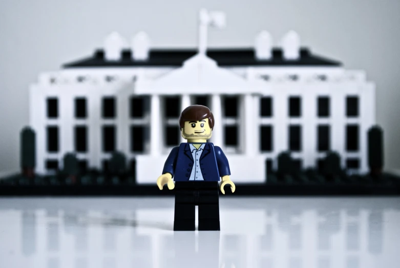 a lego person stands near a model of the white house