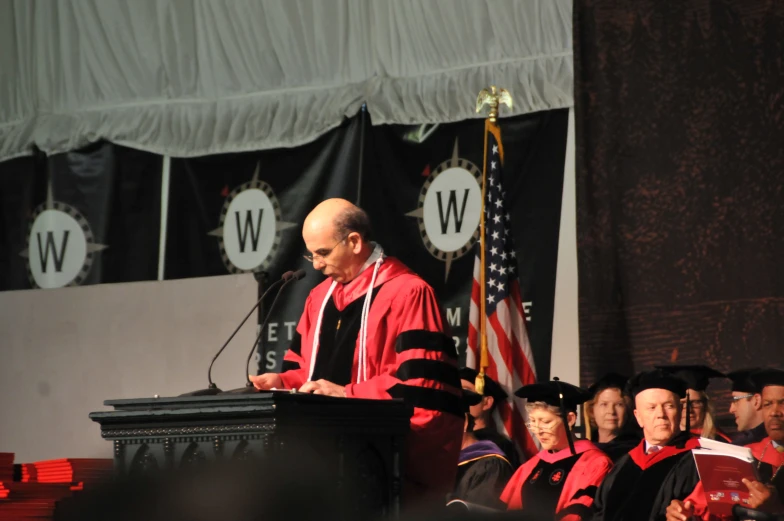 a graduate standing at a podium speaking to his peers