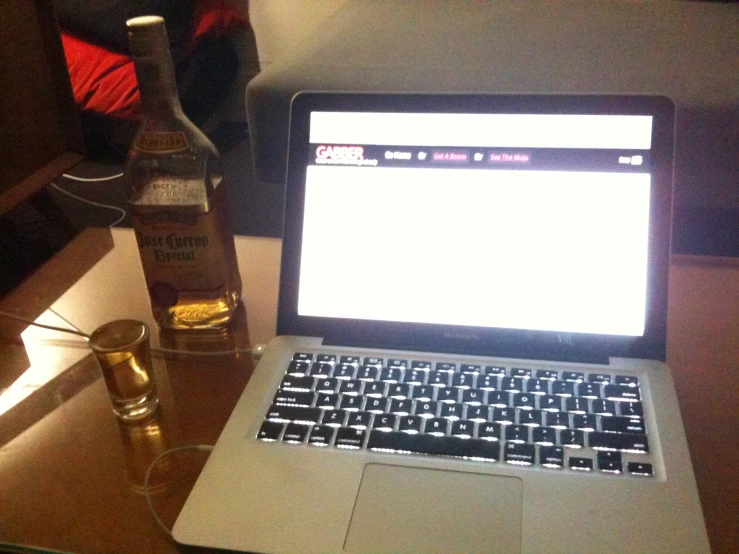 an open laptop computer sitting on a table with a bottle of whisky in front of it