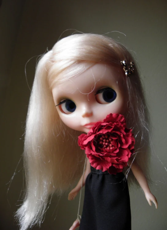 a doll with blonde hair and a red flower in her mouth
