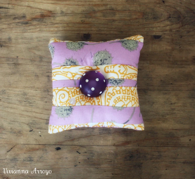 a purple and yellow pillow with an orange decorative on on the front