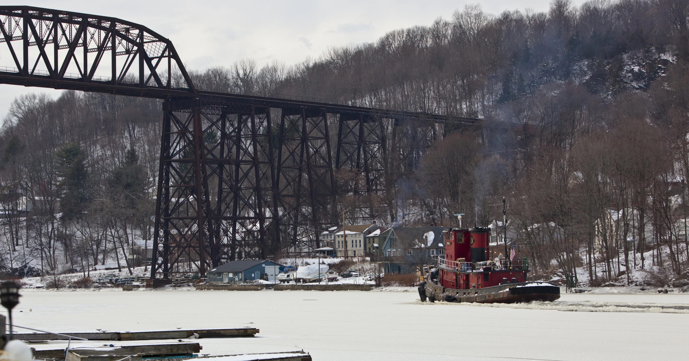 a snowy landscape shows an old train bridge that is hanging over water