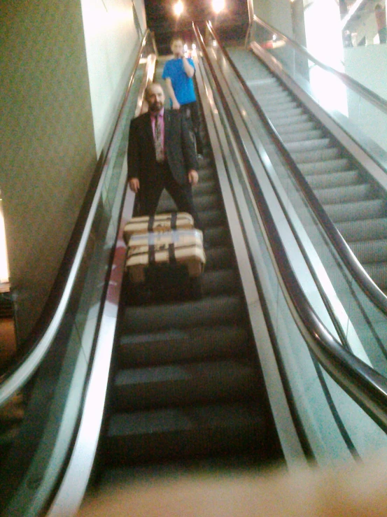 two men standing on the escalator with luggage