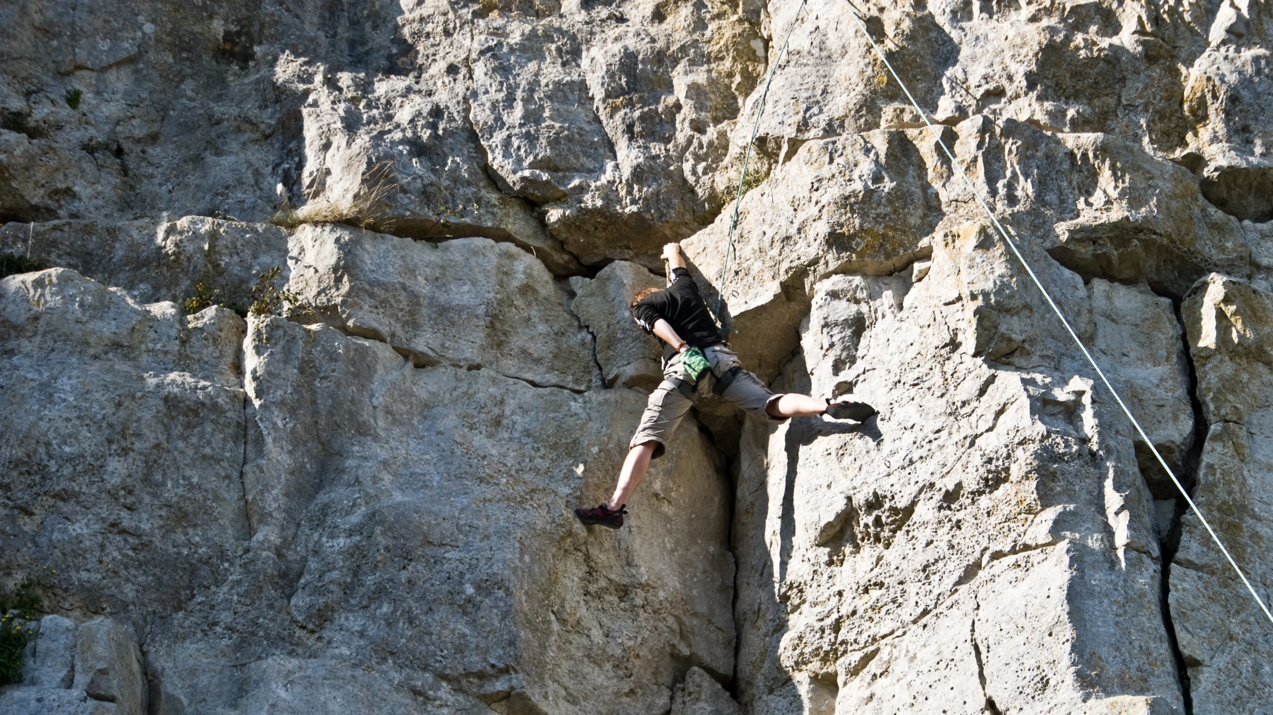 person with climbing gear on climbing up a steep rock face