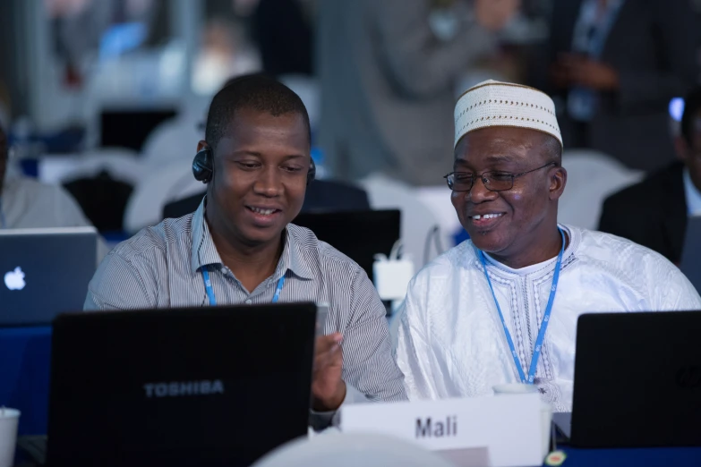 two men sitting in front of laptops in a room