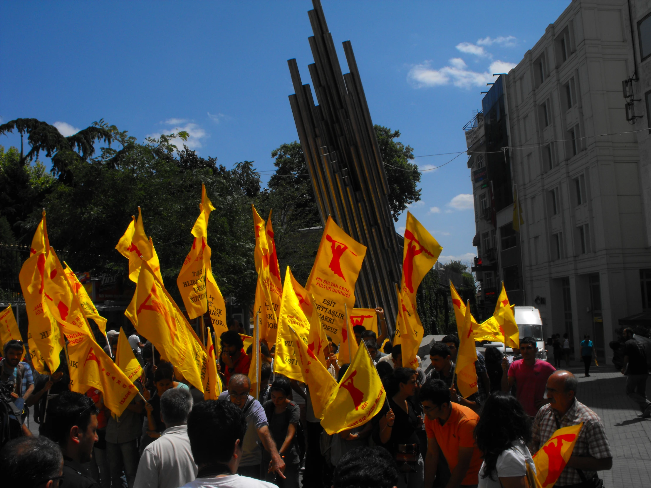 a crowd of people standing around a crowd with yellow flags