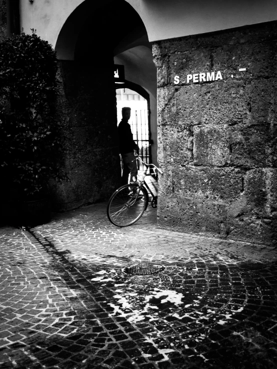 man holding up his bike through an arched doorway