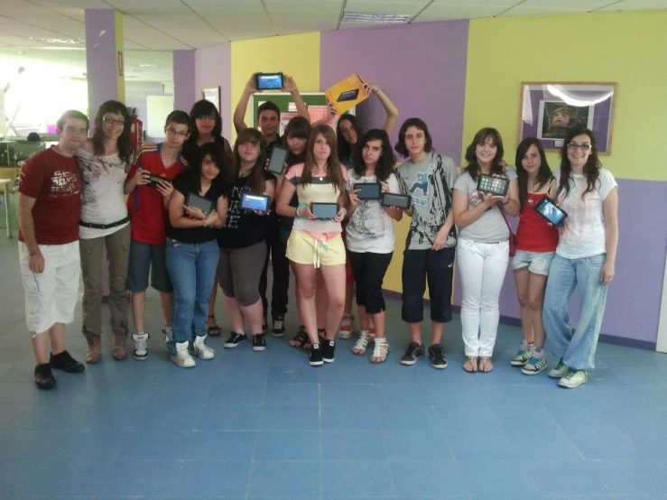 group po of young people holding electronics in front of multicolored room